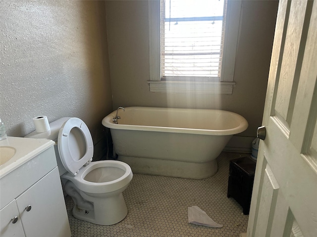 full bathroom with toilet, a freestanding tub, a textured wall, and vanity