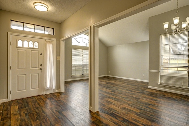 foyer with a textured ceiling, a chandelier, lofted ceiling, baseboards, and dark wood-style floors