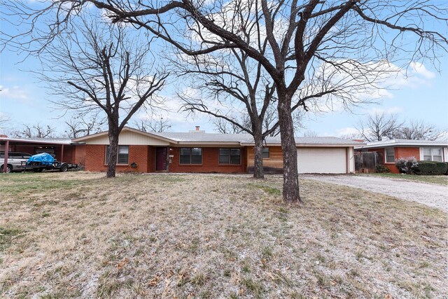 single story home with driveway, a chimney, an attached garage, a front lawn, and brick siding