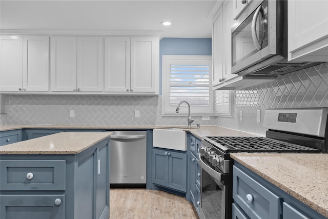 kitchen with a sink, white cabinetry, blue cabinetry, appliances with stainless steel finishes, and light wood-type flooring