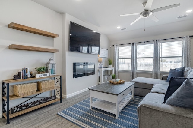 living area featuring a glass covered fireplace, wood finished floors, visible vents, and baseboards