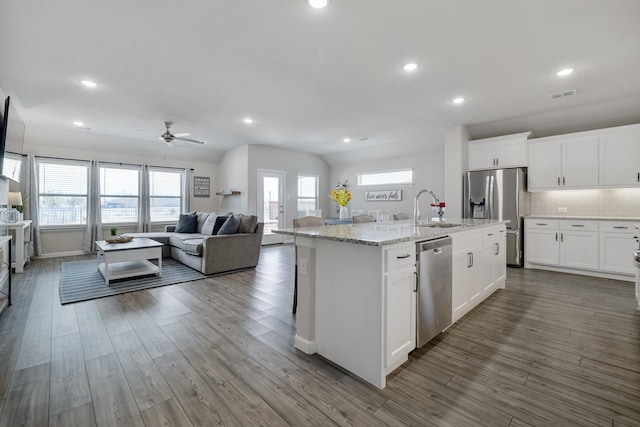 kitchen with visible vents, appliances with stainless steel finishes, open floor plan, a kitchen island with sink, and white cabinetry