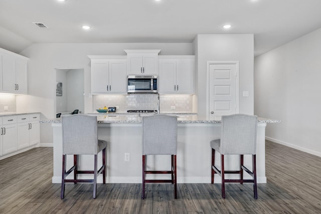 kitchen with a center island with sink, stainless steel microwave, white cabinets, and a breakfast bar area