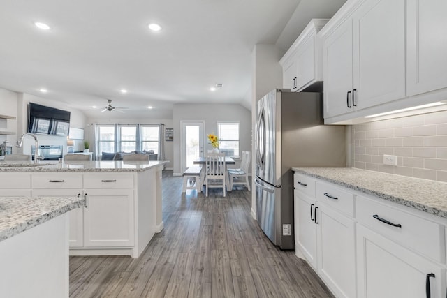 kitchen featuring open floor plan, light stone counters, a sink, and white cabinetry