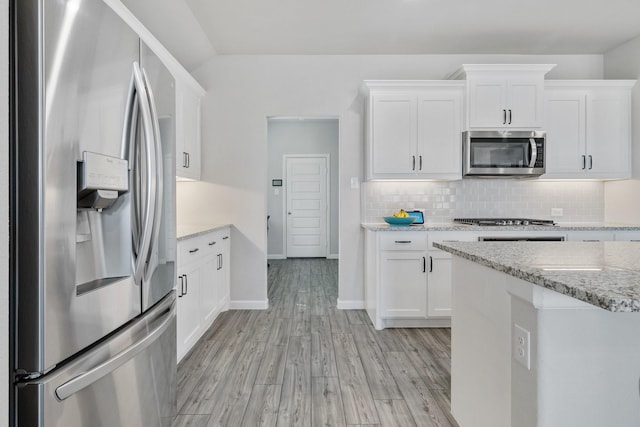 kitchen with light wood-style floors, white cabinets, appliances with stainless steel finishes, backsplash, and light stone countertops