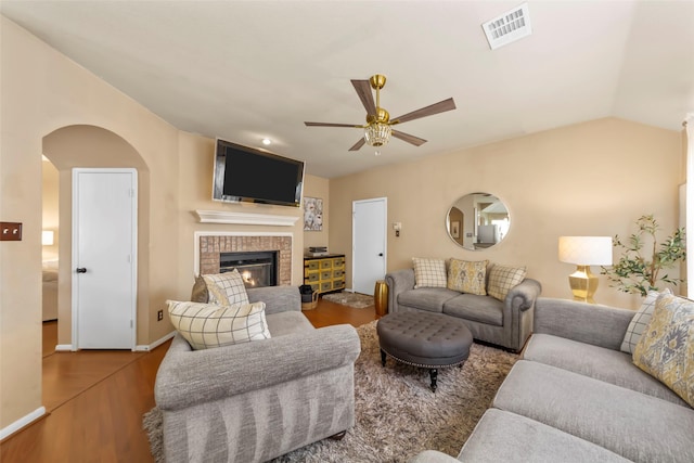 living area featuring a ceiling fan, wood finished floors, a fireplace, baseboards, and arched walkways