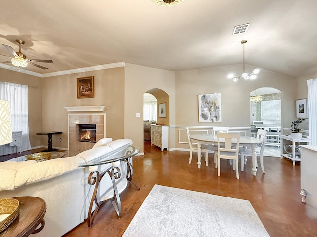 living room with lofted ceiling, arched walkways, a tile fireplace, ceiling fan with notable chandelier, and visible vents