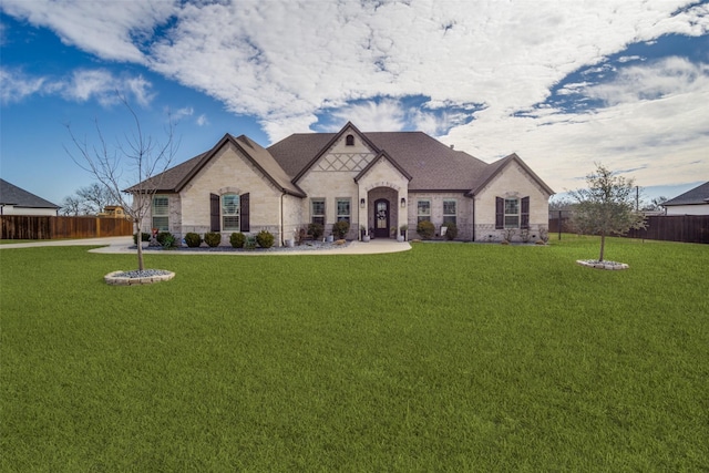 french country style house featuring stone siding, fence, and a front yard