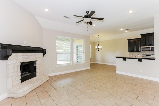 unfurnished living room featuring ceiling fan with notable chandelier, a stone fireplace, visible vents, and baseboards