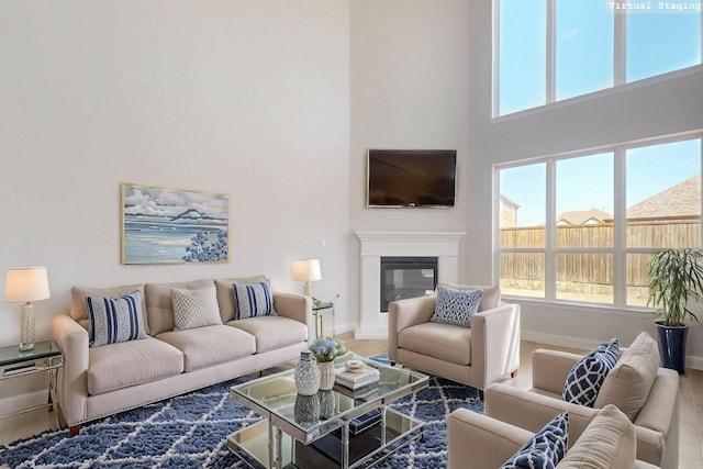 living room featuring a healthy amount of sunlight, a towering ceiling, baseboards, and a glass covered fireplace