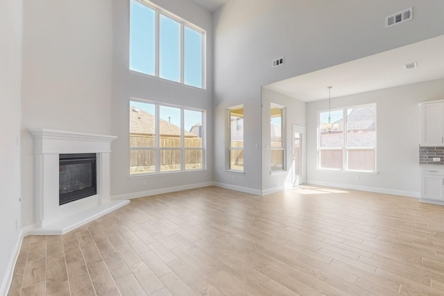 unfurnished living room with light wood finished floors, plenty of natural light, a glass covered fireplace, and visible vents