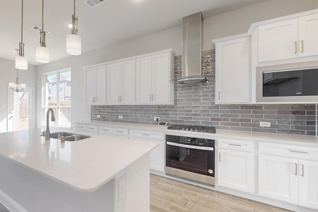 kitchen featuring stainless steel appliances, light countertops, white cabinets, a sink, and wall chimney exhaust hood