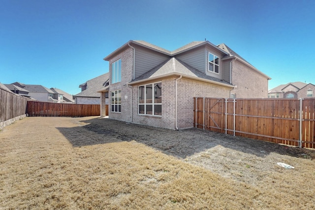 back of house with a fenced backyard, a lawn, and brick siding