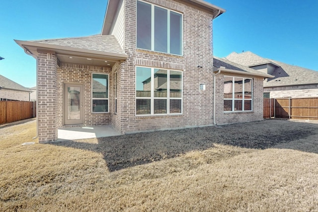 rear view of house with roof with shingles, brick siding, fence, and a patio