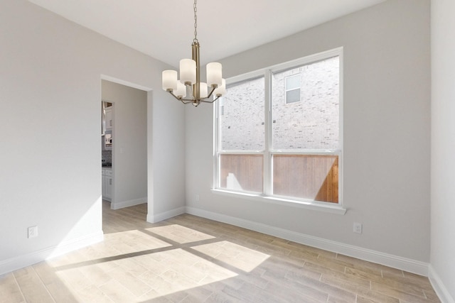 unfurnished dining area featuring a chandelier, light wood-type flooring, and baseboards