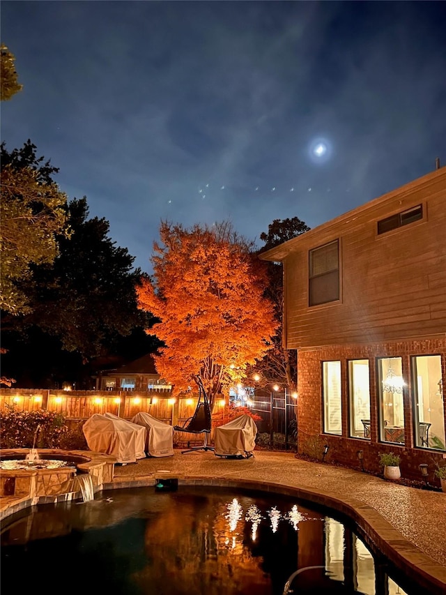 pool at twilight featuring an outdoor pool, a fenced backyard, and a hot tub