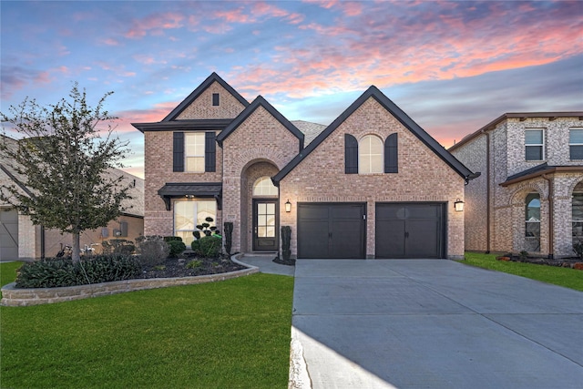 french provincial home featuring a garage, a yard, concrete driveway, and brick siding