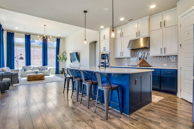 kitchen featuring a center island with sink, light countertops, open floor plan, white cabinetry, and under cabinet range hood