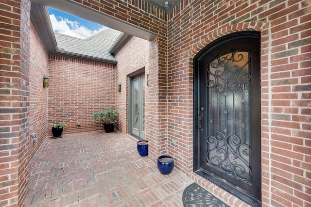 view of exterior entry featuring brick siding and a shingled roof