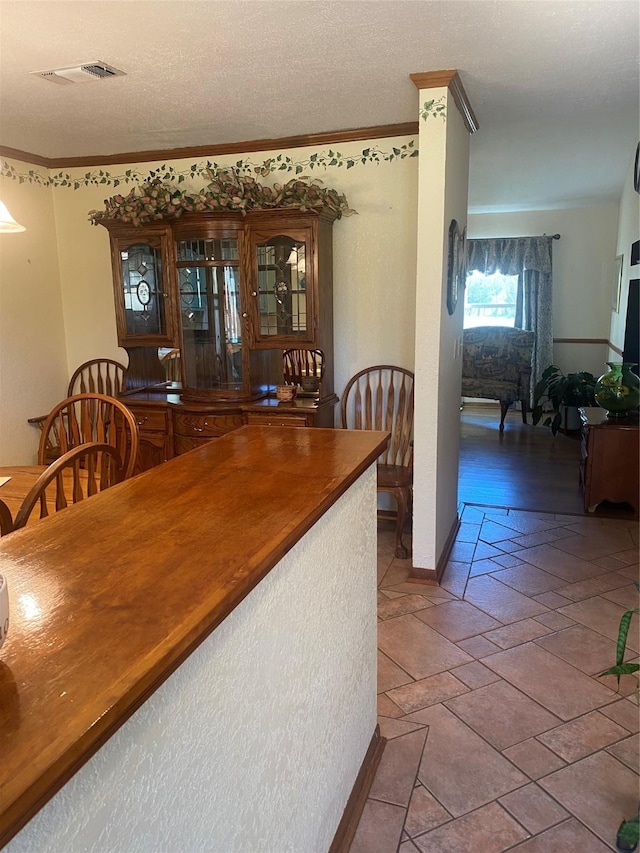 dining room with a textured ceiling, ornamental molding, visible vents, and baseboards