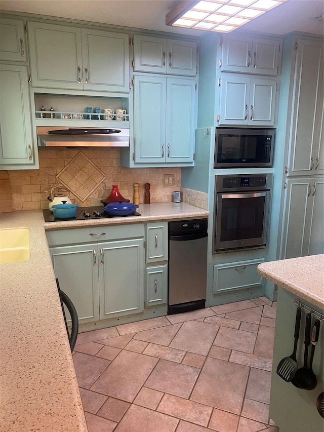 kitchen with under cabinet range hood, appliances with stainless steel finishes, a sink, and tasteful backsplash