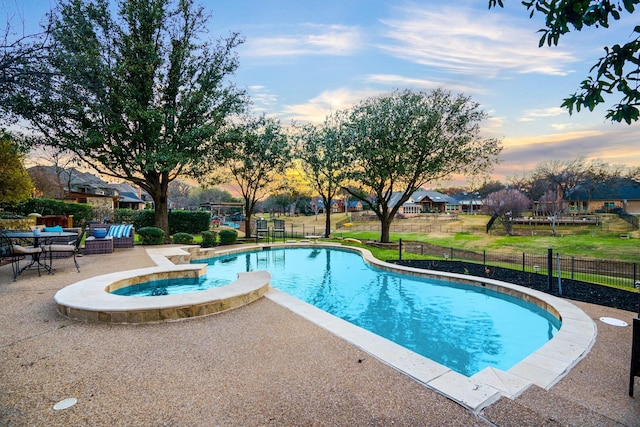 pool at dusk with a patio area, fence, and a pool with connected hot tub