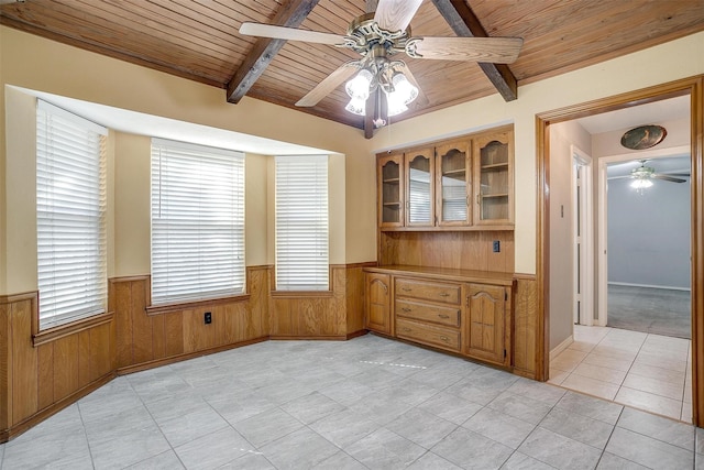 empty room featuring wooden walls, wooden ceiling, a wainscoted wall, ceiling fan, and beamed ceiling