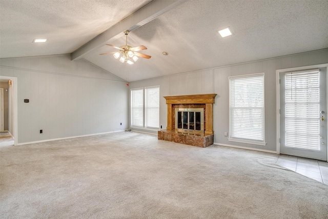 unfurnished living room with lofted ceiling with beams, ceiling fan, a textured ceiling, light colored carpet, and a tiled fireplace