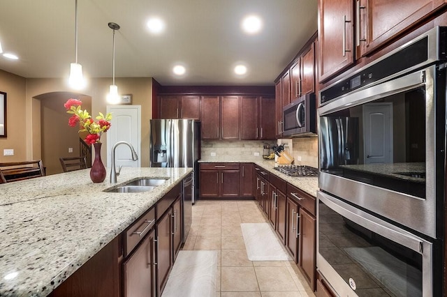 kitchen featuring a sink, hanging light fixtures, appliances with stainless steel finishes, light stone countertops, and tasteful backsplash