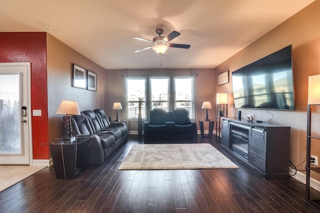 living room featuring ceiling fan, baseboards, and dark wood-type flooring