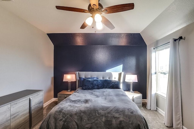 carpeted bedroom featuring an accent wall, vaulted ceiling, baseboards, and ceiling fan