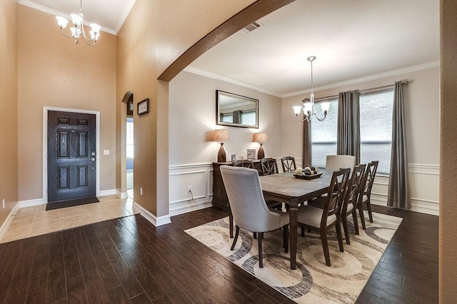 dining area featuring arched walkways, a wainscoted wall, wood finished floors, crown molding, and a chandelier