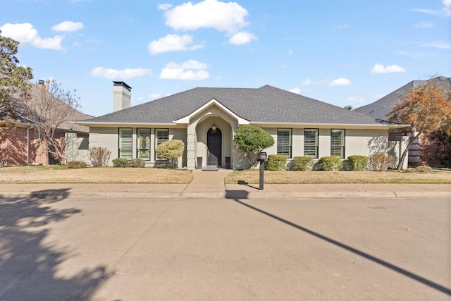 ranch-style house featuring a shingled roof, a chimney, and a front lawn