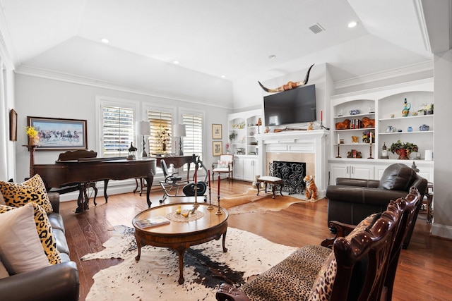 living area featuring built in features, lofted ceiling, visible vents, a premium fireplace, and wood finished floors