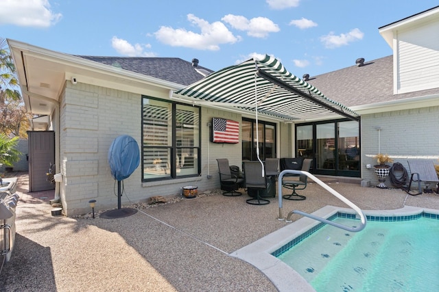 rear view of house with a patio area, roof with shingles, an outdoor pool, and brick siding