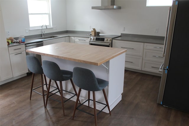 kitchen featuring stainless steel appliances, wall chimney range hood, a kitchen bar, white cabinetry, and a sink