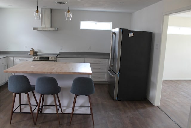 kitchen featuring a breakfast bar, pendant lighting, appliances with stainless steel finishes, white cabinets, and wall chimney exhaust hood