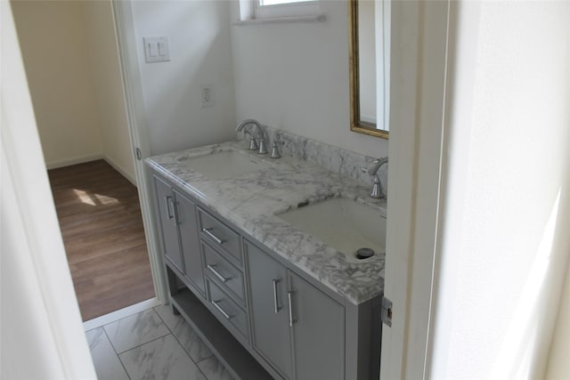 full bath with marble finish floor, a sink, baseboards, and double vanity