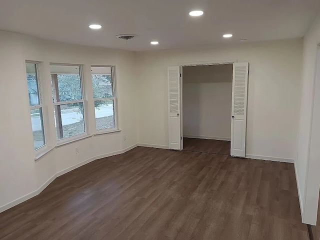 empty room featuring visible vents, baseboards, dark wood-type flooring, and recessed lighting