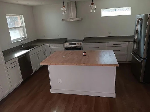 kitchen featuring wall chimney exhaust hood, appliances with stainless steel finishes, a center island, hanging light fixtures, and a sink