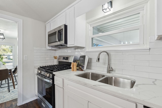 kitchen with light stone countertops, appliances with stainless steel finishes, white cabinets, and a sink