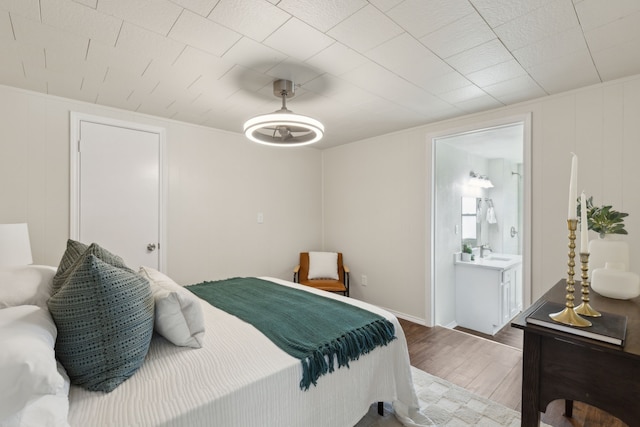 bedroom featuring a ceiling fan, a sink, ensuite bath, and wood finished floors