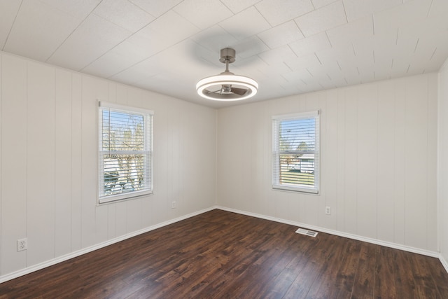 spare room featuring a wealth of natural light, visible vents, baseboards, and dark wood-type flooring