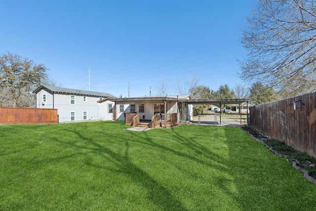 rear view of house with an attached carport, a fenced backyard, a yard, and a deck