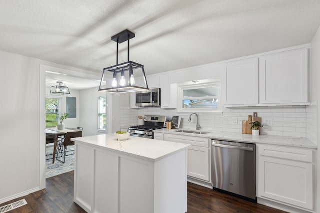 kitchen featuring visible vents, decorative backsplash, a kitchen island, stainless steel appliances, and a sink