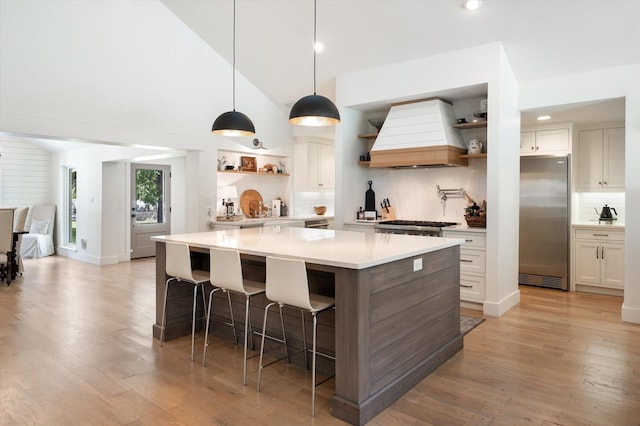 kitchen with white cabinets, custom range hood, a breakfast bar area, light countertops, and open shelves