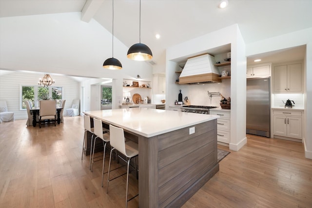 kitchen with custom exhaust hood, open shelves, light countertops, light wood-style flooring, and stainless steel fridge