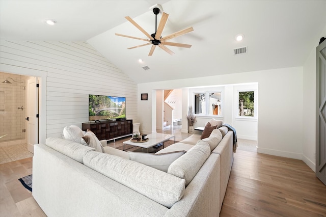 living room with light wood finished floors, lofted ceiling, visible vents, ceiling fan, and stairs