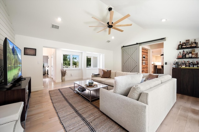 living room with lofted ceiling, a barn door, light wood-style flooring, visible vents, and a ceiling fan