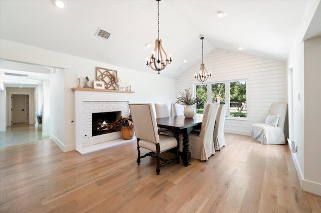 dining area featuring light wood finished floors, visible vents, lofted ceiling, a fireplace, and a chandelier